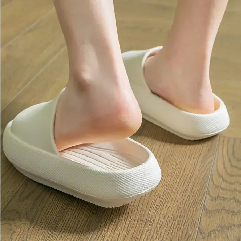 A close-up of feet slipping into CozySteps Unisex EVA Beach & Bathroom Flip-Flops by CozySteps.uk, US sizes 6–12. These beige flip-flops feature textured, non-slip soles and offer cushioned comfort on wooden floors.