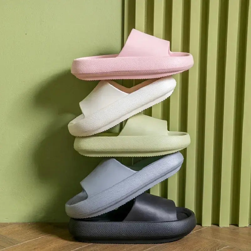 Four pairs of CozySteps Unisex EVA Beach & Bathroom Flip-Flops (US 6–12) by CozySteps.uk in pink, white, light green, gray, and black are stacked vertically against a textured green wall on a wooden floor.