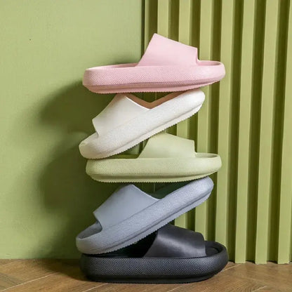 Four pairs of CozySteps Unisex EVA Beach & Bathroom Flip-Flops (US 6–12) by CozySteps.uk in pink, white, light green, gray, and black are stacked vertically against a textured green wall on a wooden floor.